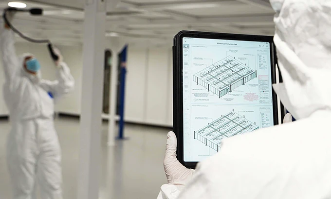 Two technicians in protective suits are checking the cleanroom per the layout drawings.