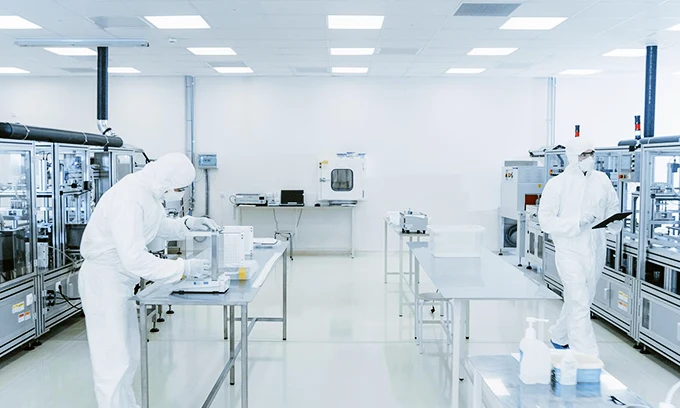 Two persons wearing protective clothing are working in a cleanroom.