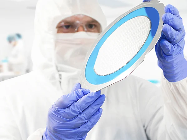 A person wearing protective clothing is inspecting a wafer.