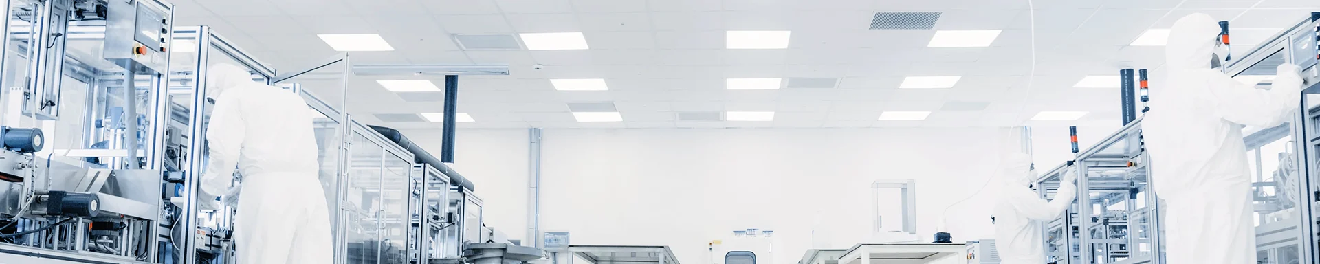 Three persons in protective suits are working in a cleanroom.