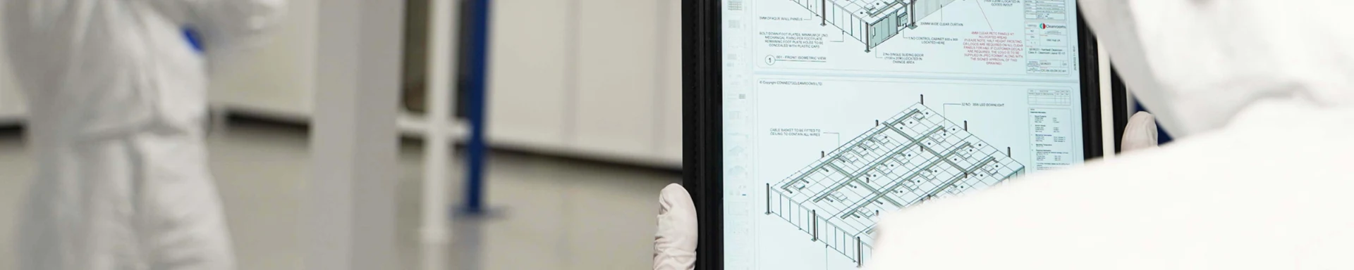 Two technicians in protective suits are checking the cleanroom per the layout drawings.