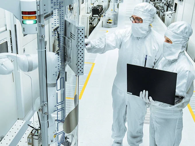 Two persons in protective clothing are discussing in a cleanroom with a computer.