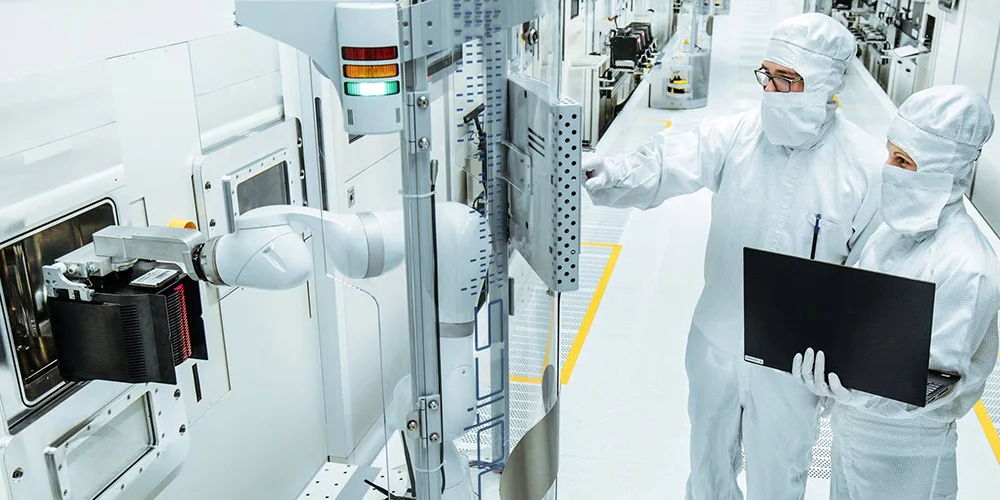 Two persons in protective clothing are discussing in a cleanroom with a computer.