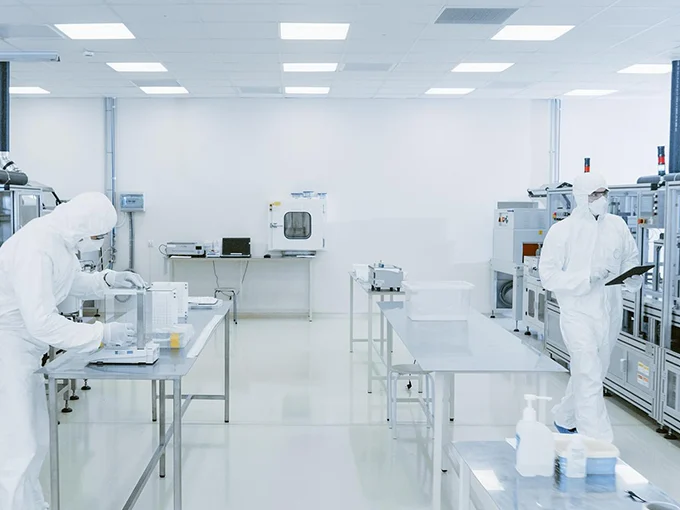 2 persons wearing protective suits are working in a cleanroom.