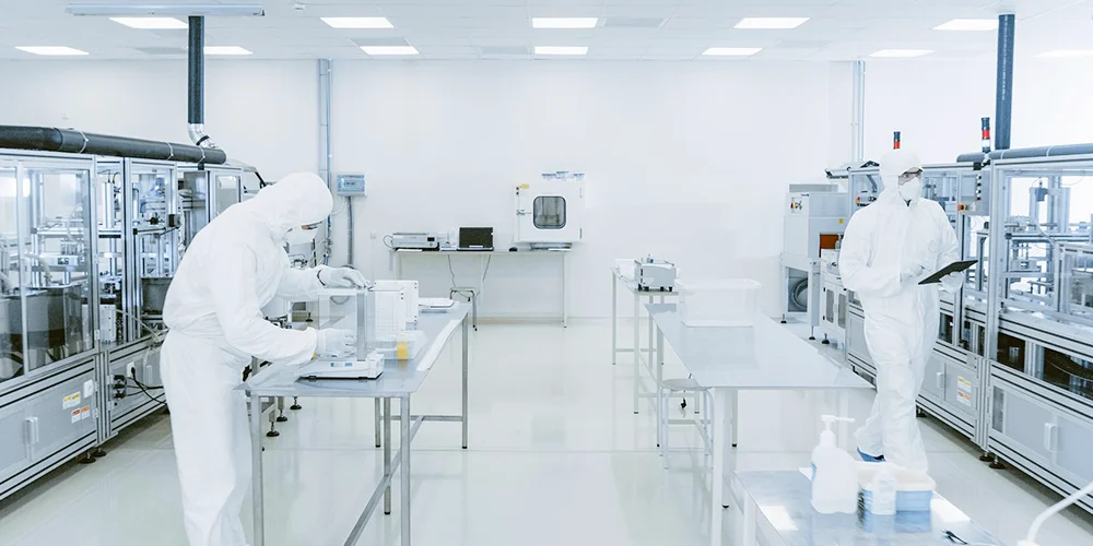 2 persons wearing protective suits are working in a cleanroom.
